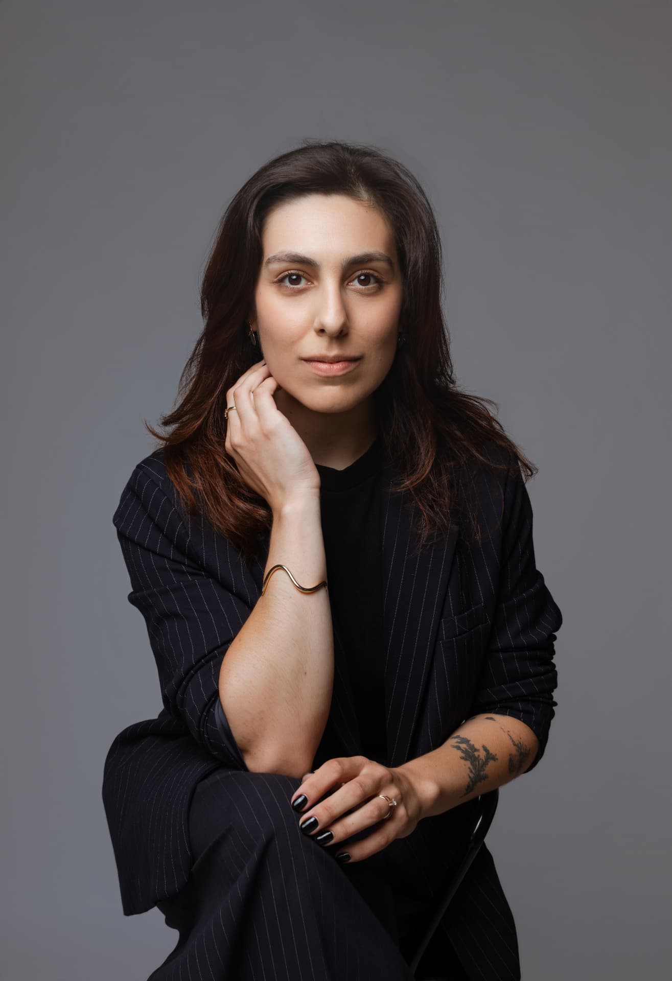 Retrato de Sabrina Rodrigues sentada, em estúdio com fundo cinza